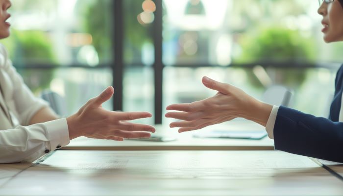 Two people sitting across from each other conversing and using their hands as they talk